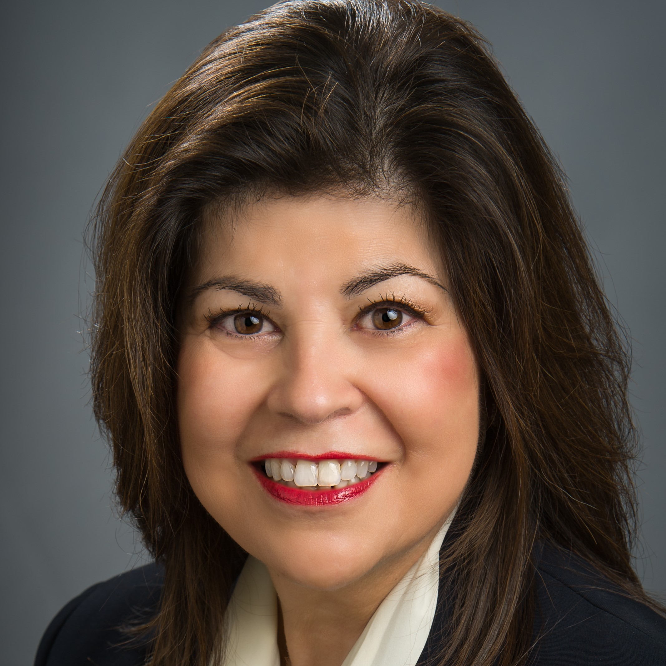 Photo of Rufina Hernández, a Latina woman wearing a blue suit with white shirt, has brown eyes and long dark brown hair. She is smiling.